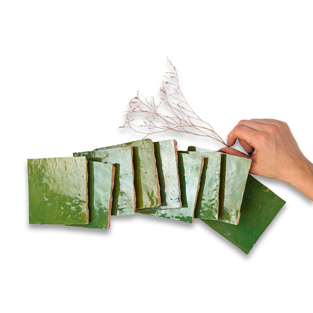 Hand arranging dried branches on a set of green ceramic tiles against a white background