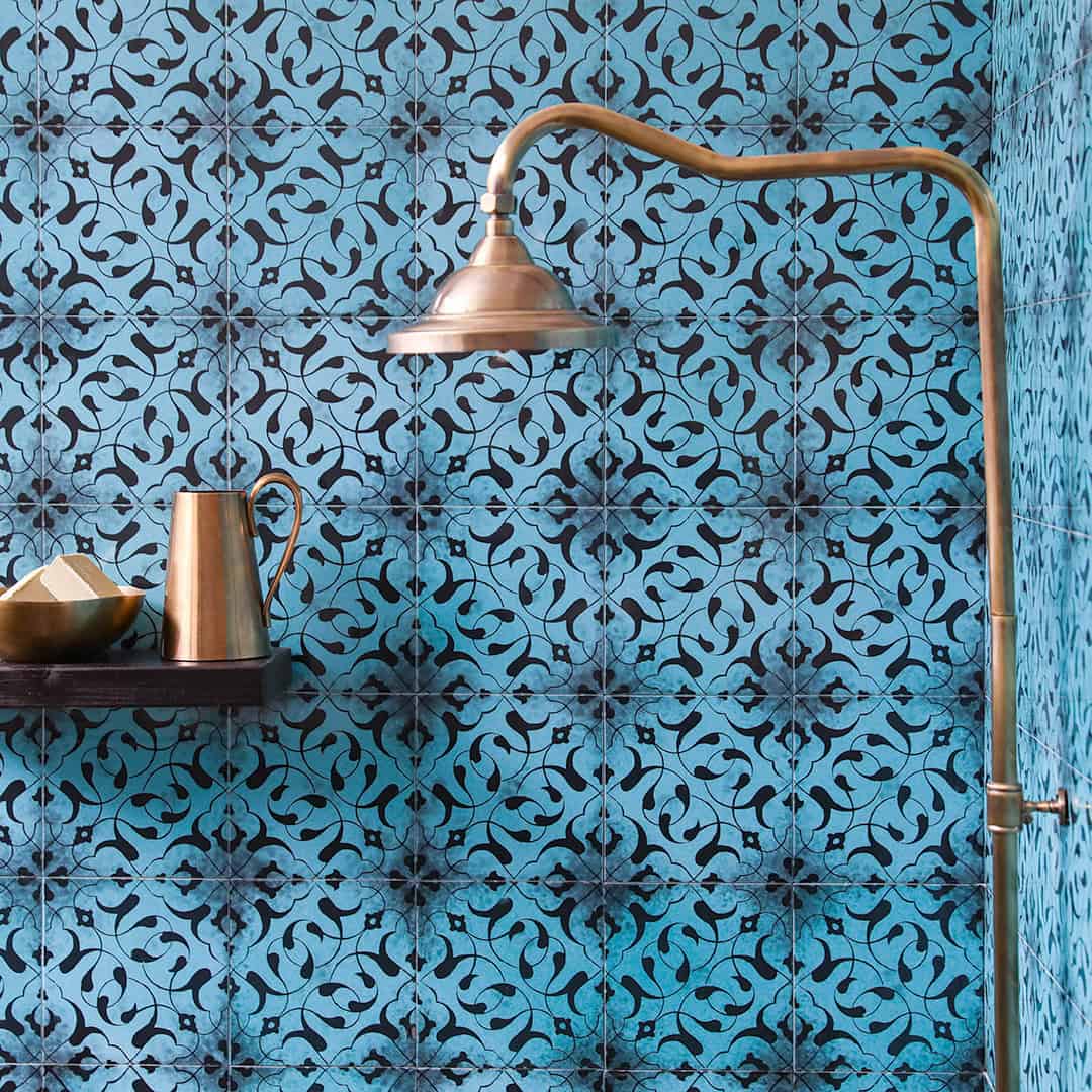 Turquoise patterned tile wall with brass shower fixture and wooden shelf holding copper vessels.