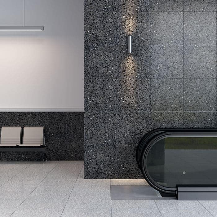 Modern interior with dark terrazzo wall, sleek wall sconce lighting, and escalator beside light gray terrazzo flooring.
