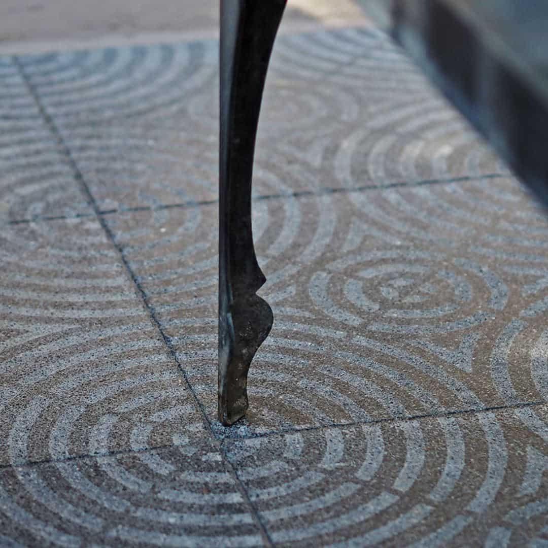 A square cement tile featuring a textured gray surface with concentric circular patterns intersecting at the center, creating a geometric, symmetrical, and modern decorative design.
