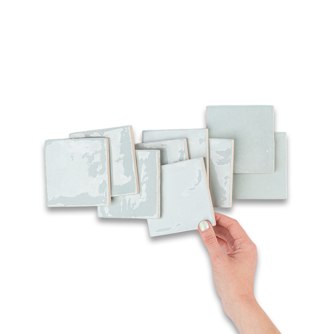 Hand holding a set of light gray ceramic tiles with a marble-like texture on a white background.