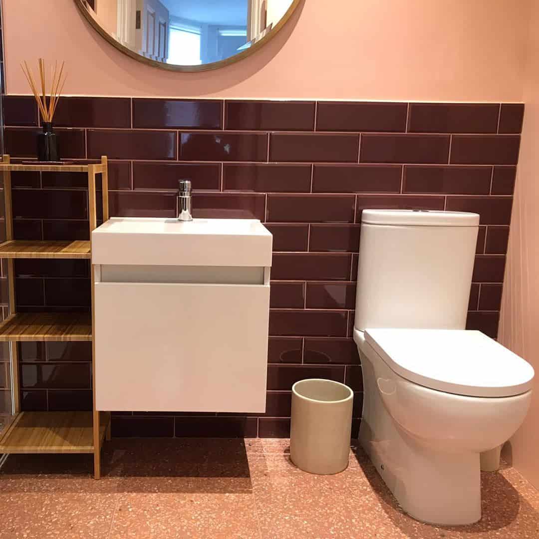 Small bathroom with burgundy subway tiles, floating vanity, modern toilet, terrazzo floor, and light wood shelving unit.