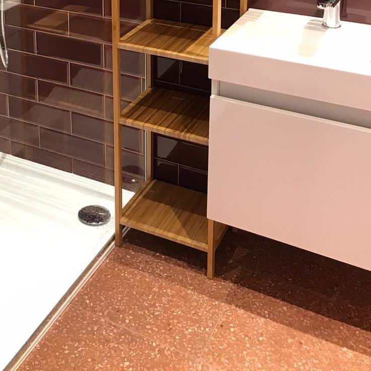 Small bathroom with burgundy subway tiles, floating vanity, modern toilet, terrazzo floor, and light wood shelving unit.