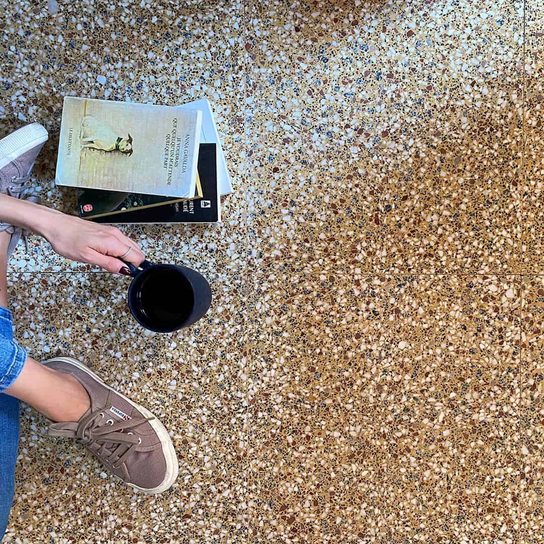 Warm-toned terrazzo tile floor with brown and cream chips, styled with sneakers and wood table edge.