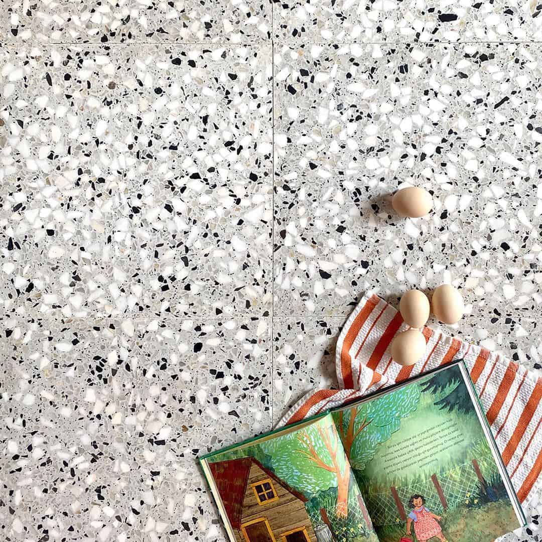Light gray terrazzo surface with eggs, striped cloth, and open illustrated book arranged in kitchen scene.