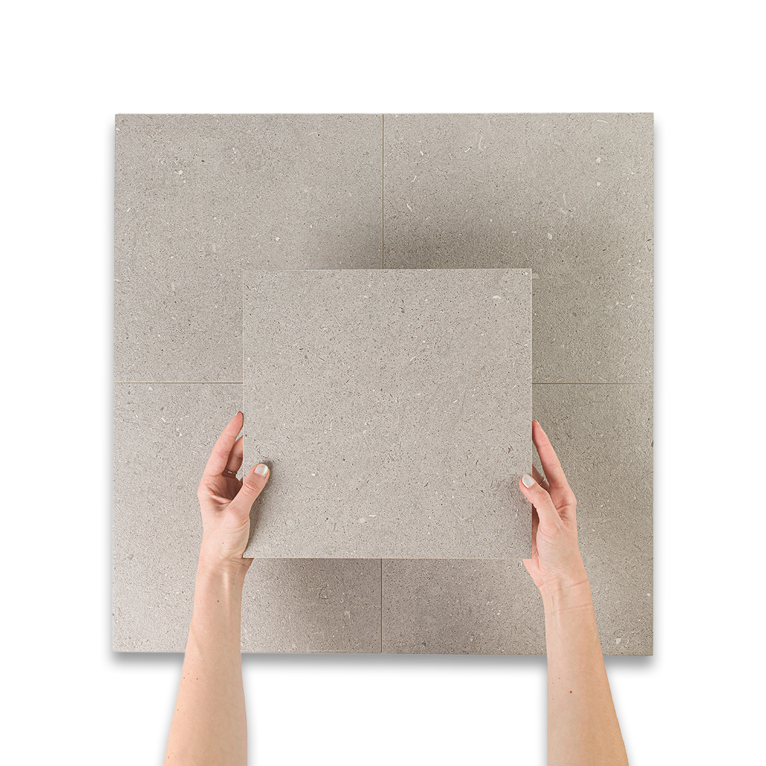 Two hands holding a square piece of gray tile with cement texture.