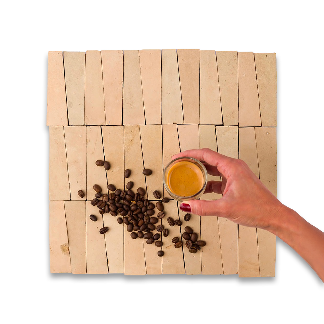Hand holding a small jar of coffee over coffee beans on a woven wooden mat.