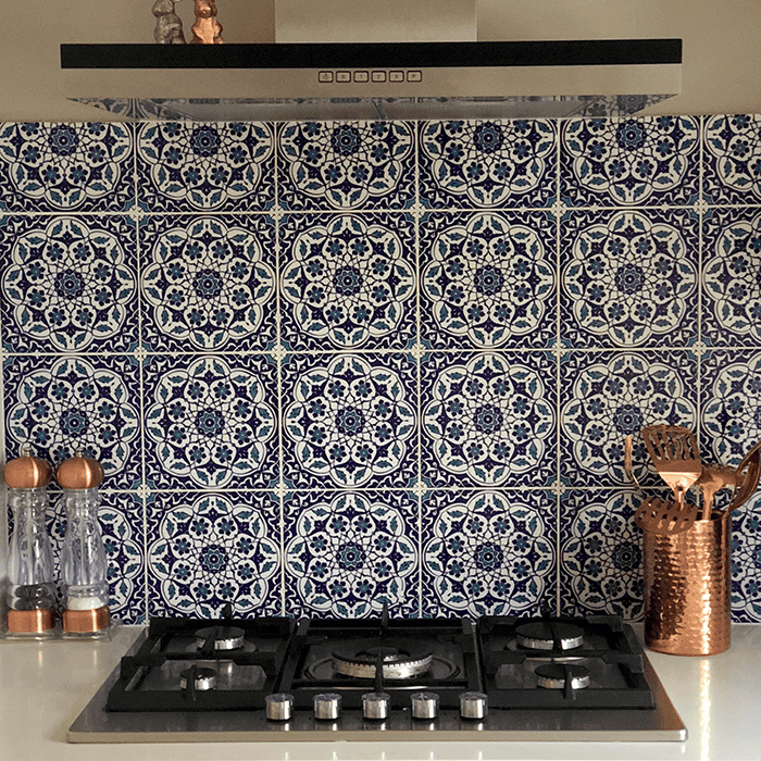 Modern kitchen with gas stovetop, stainless range hood, patterned blue tiles, and copper accents.