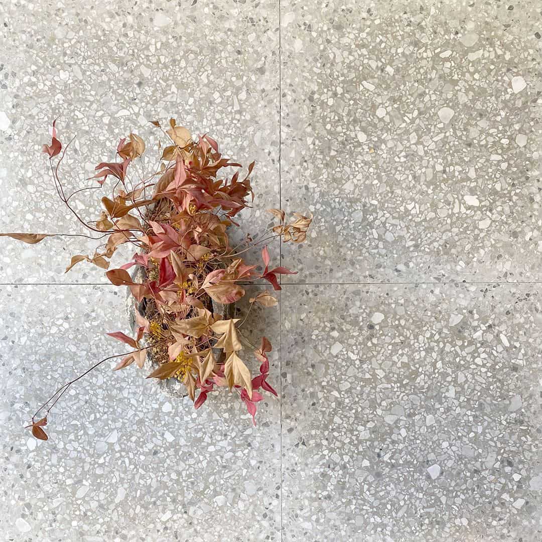 Light gray terrazzo tile floor with subtle stone chips, featuring a small arrangement of dried leaves in a vase.