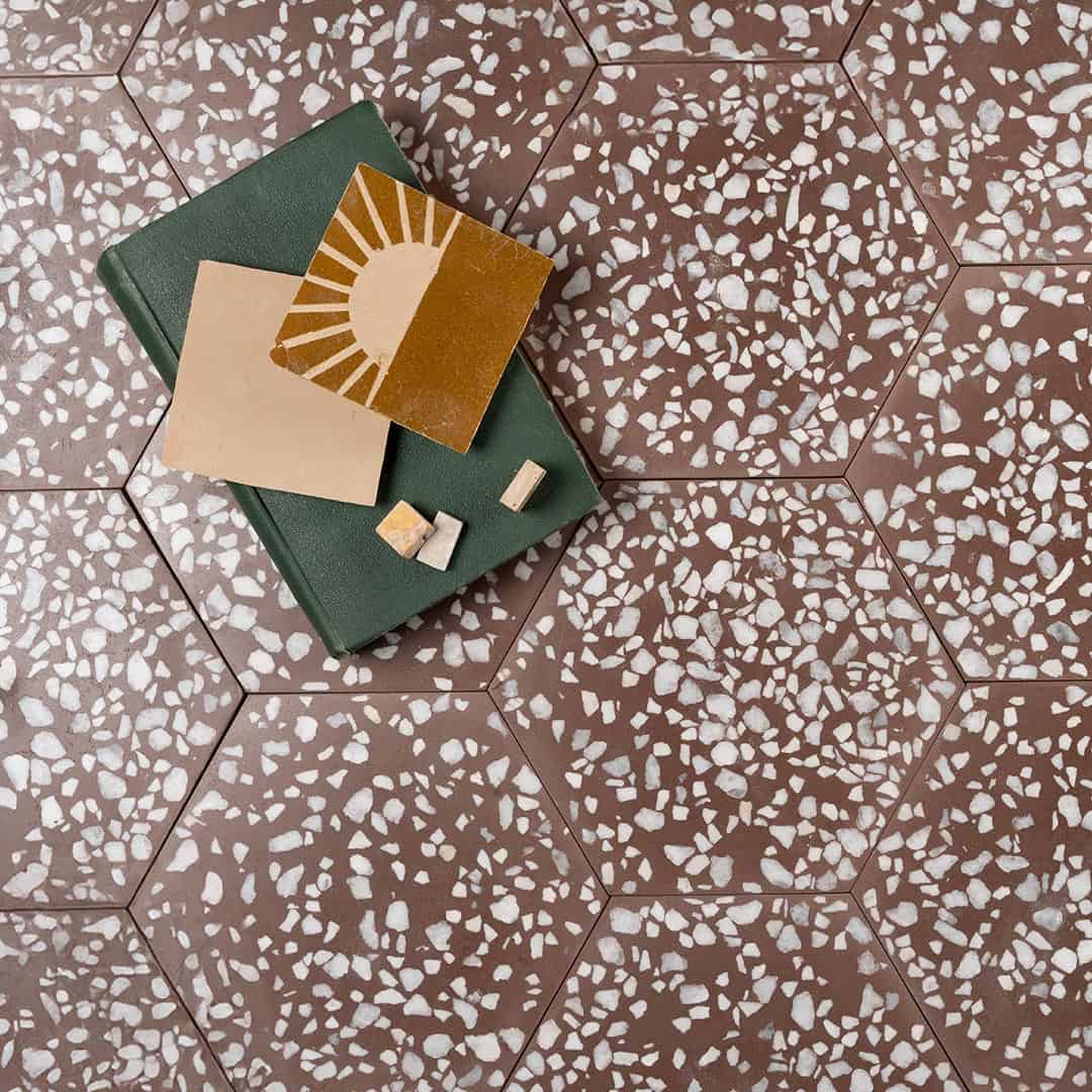 A set of hexagonal cement tiles featuring a rich brown base with scattered white terrazzo stone chips, creating a bold, modern, and textured geometric design.
