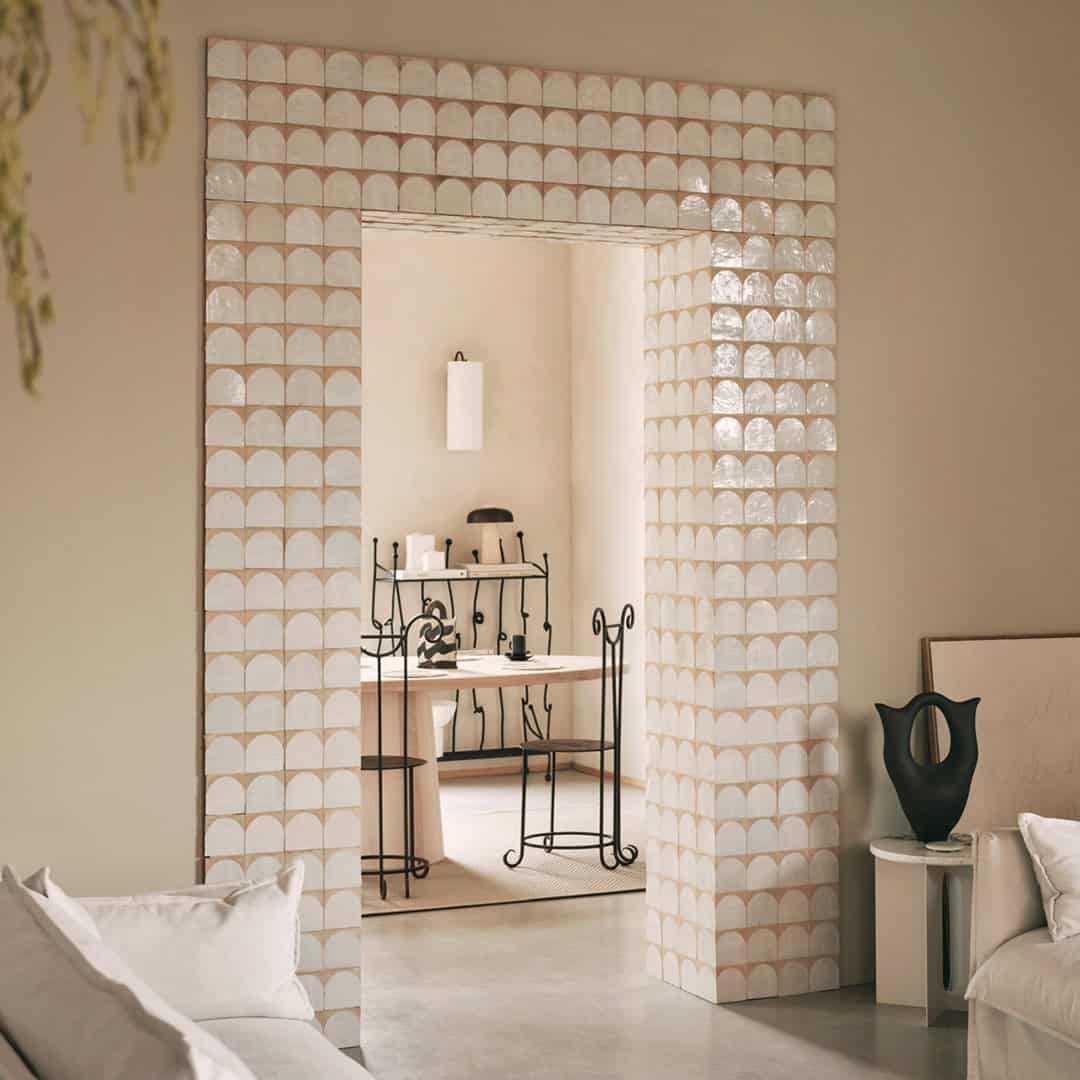 A modern interior with a doorway framed by glossy scallop-patterned tiles in soft beige and white.
