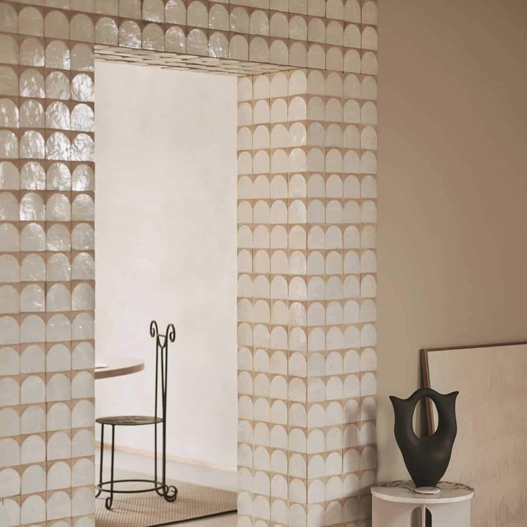 A modern interior with a doorway framed by glossy scallop-patterned tiles in soft beige and white.
