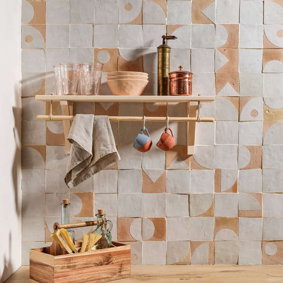 Stylish kitchen shelf with glasses, bowls, a coffee grinder, and hanging cups, against a geometric tiled wall with earthy tones.