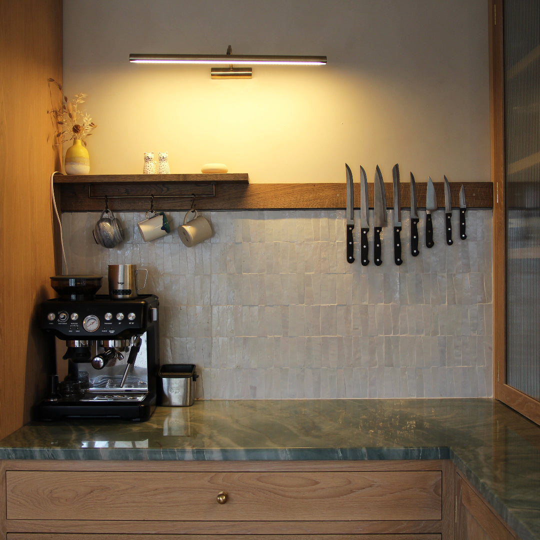 Modern kitchen with coffee machine, hanging mugs, and knife rack on a tiled wall.