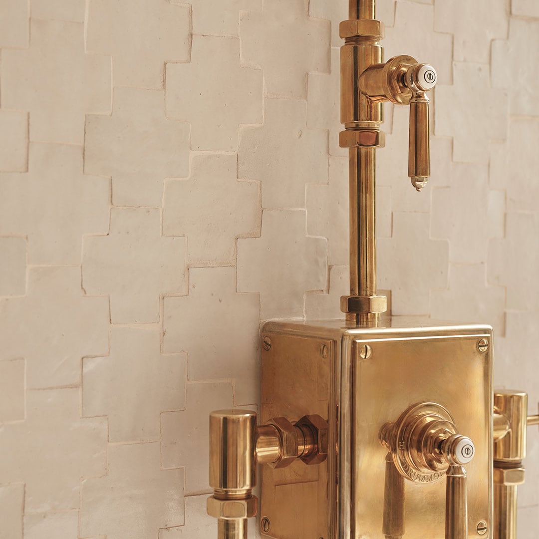Elegant copper shower fixture with rainfall head and handheld sprayer against textured neutral tile wall.