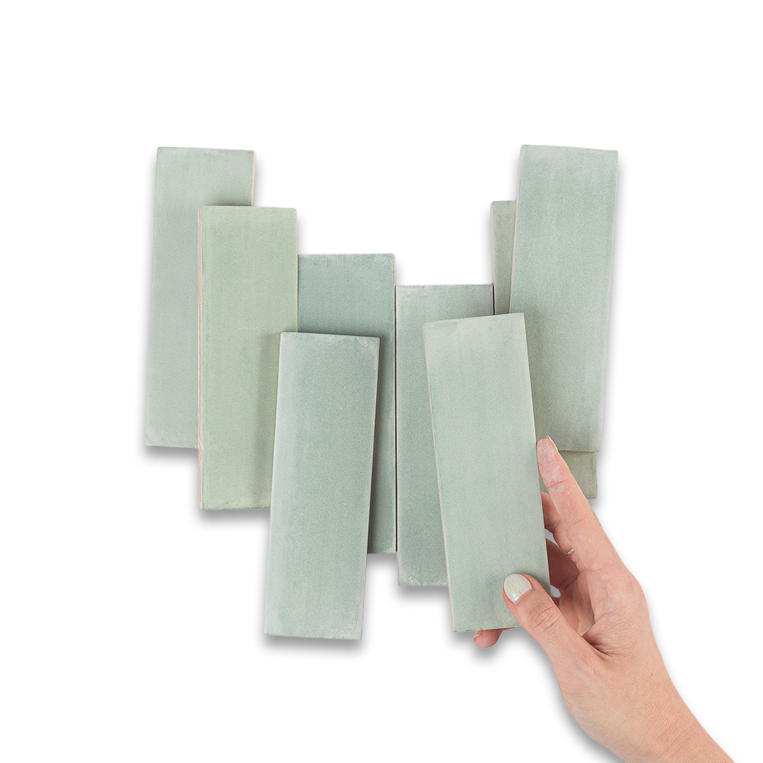 Set of light green ceramic tiles with a hand holding one tile against a white background