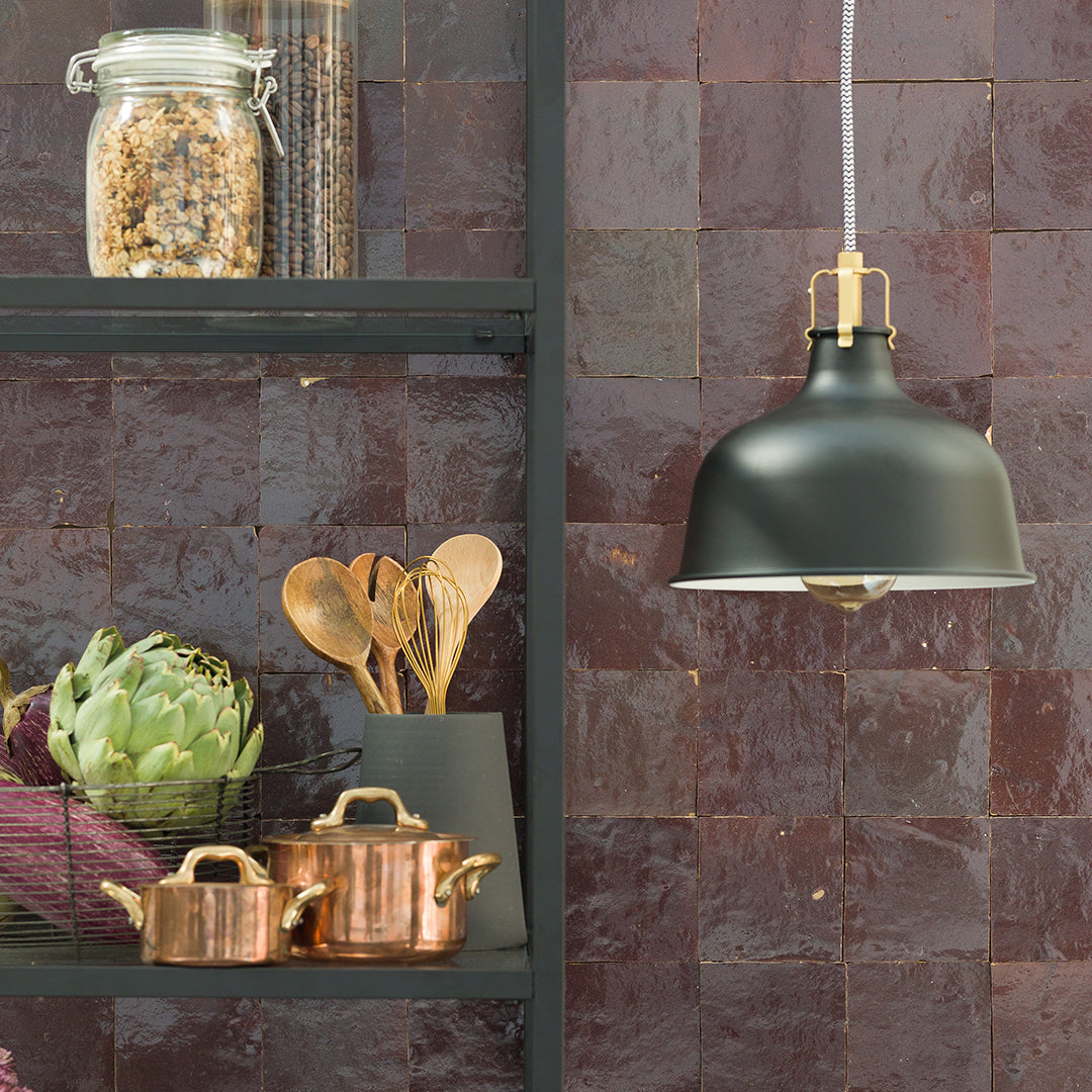 Kitchen setting with copper pots, wooden utensils, and a green pendant light on a tiled wall.