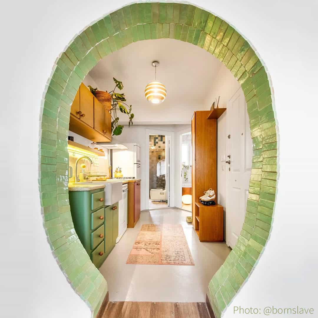 Retro kitchen with arched green tiles, warm lighting, yellow backsplash, and vintage wooden cabinets.
