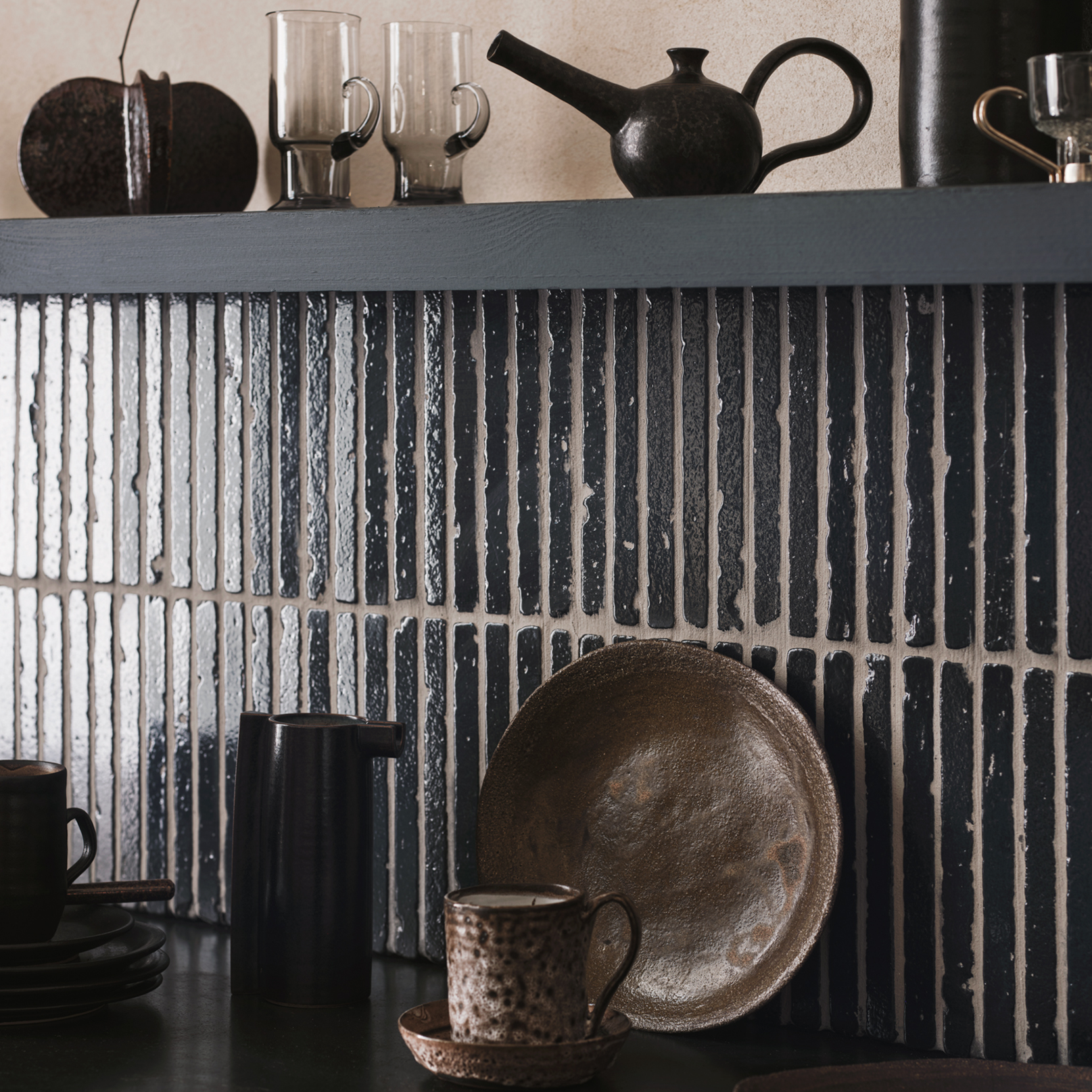 Ceramic dishes and glasses on a dark surface with a textured black and white tiled wall in the background.