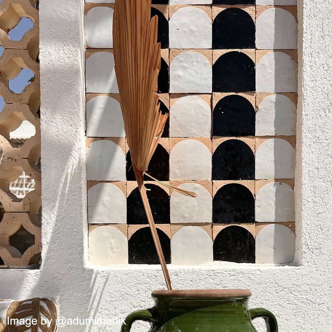 Decorative wall featuring black, white, and terracotta geometric tiles with a dried plant arrangement in a green vase.