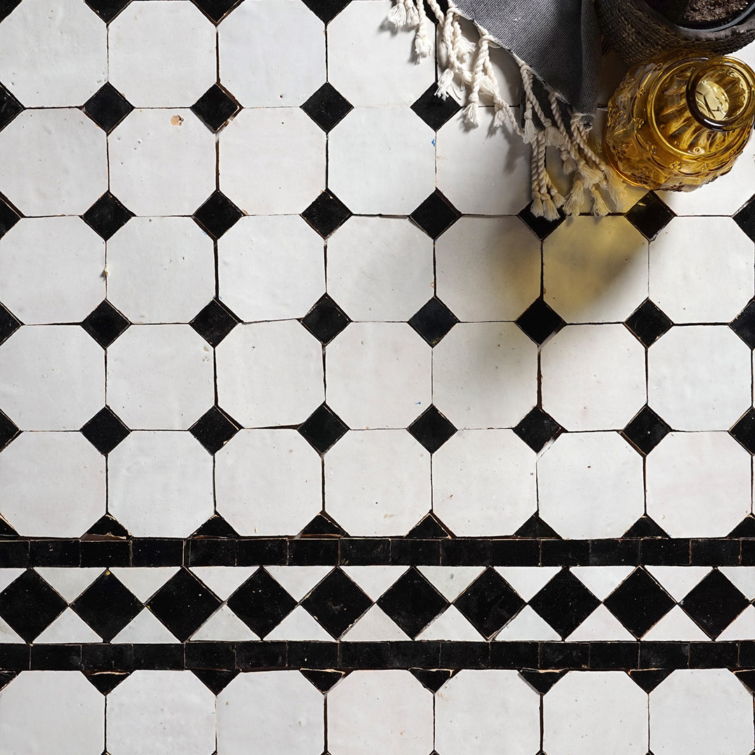 Black and white geometric tile pattern on a floor with a bottle and towel in the corner.