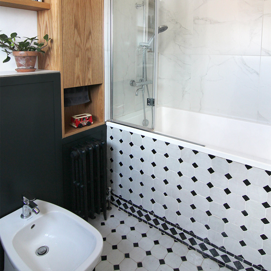 Bathroom with black and white tiled wall, sink, and wooden cabinet.