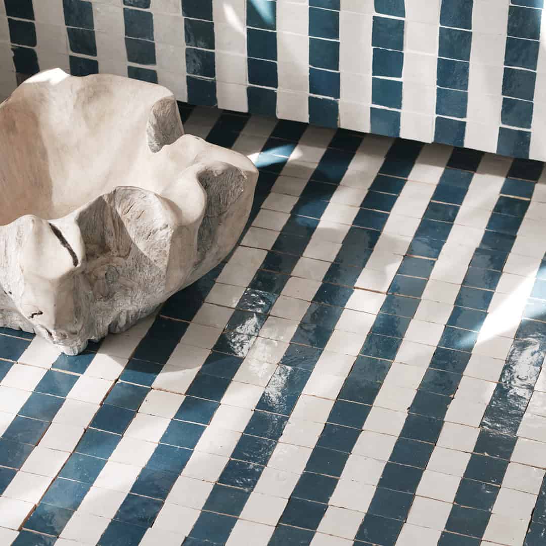Interior corner with glossy blue and white striped tiles on wall and floor, featuring large beige sculptural basin with organic shape.