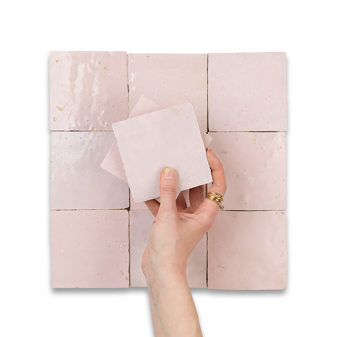 Hand holding a square tile against a patterned tile background