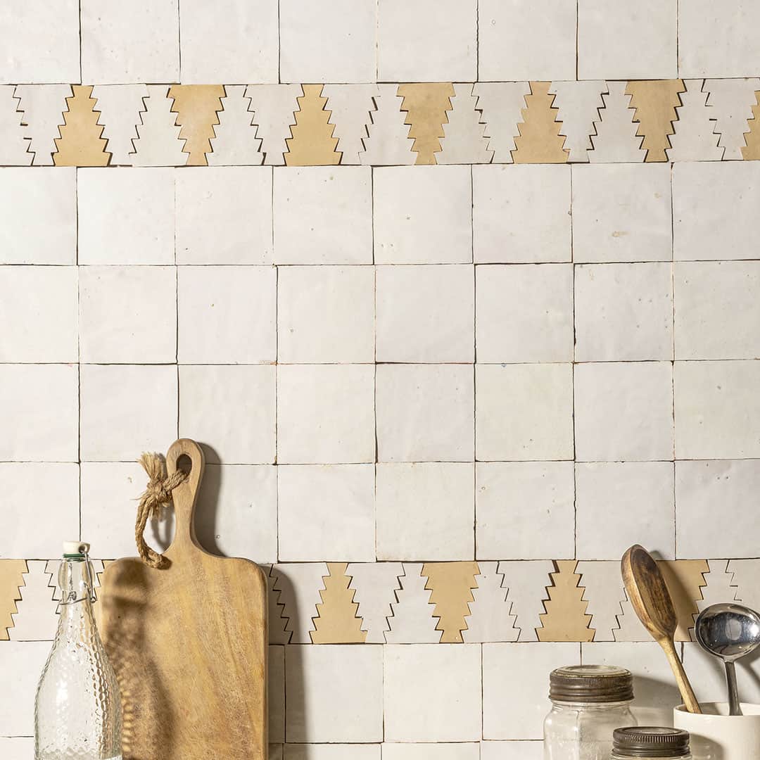 Rustic kitchen wall with off-white tiles, zigzag border, and wooden utensils in container.
