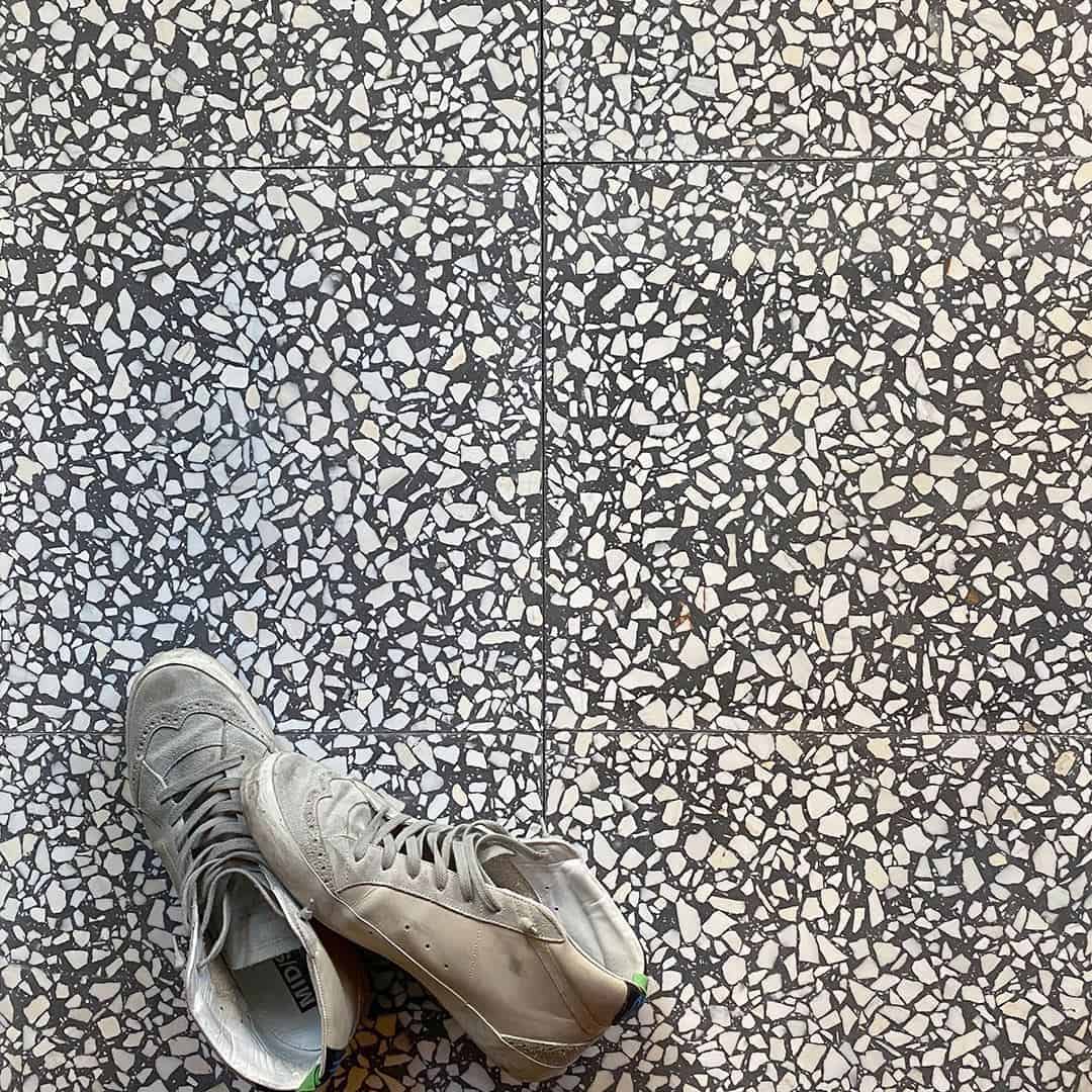 Pair of worn sneakers resting on black and white terrazzo tile floor with visible grout lines.