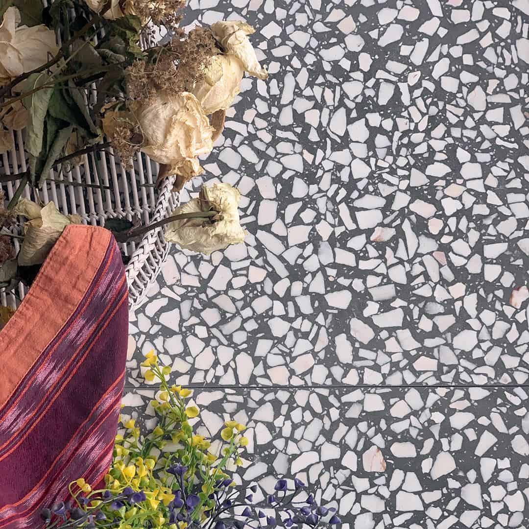 Black and white terrazzo tile floor with dried flowers, woven basket, and colorful fabric accents in corner.