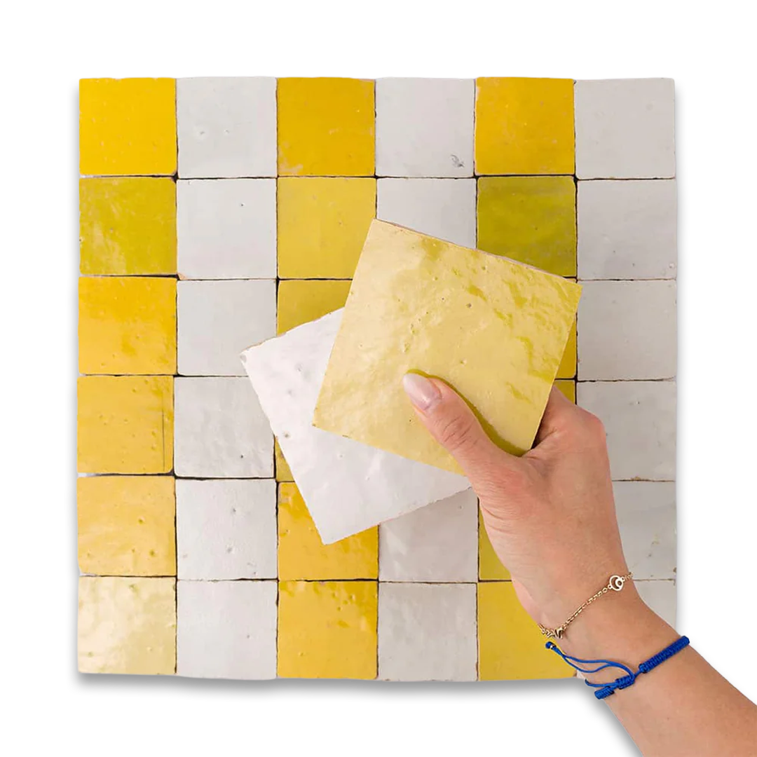 Hand holding a yellow sponge over a tiled surface with yellow and white tiles.