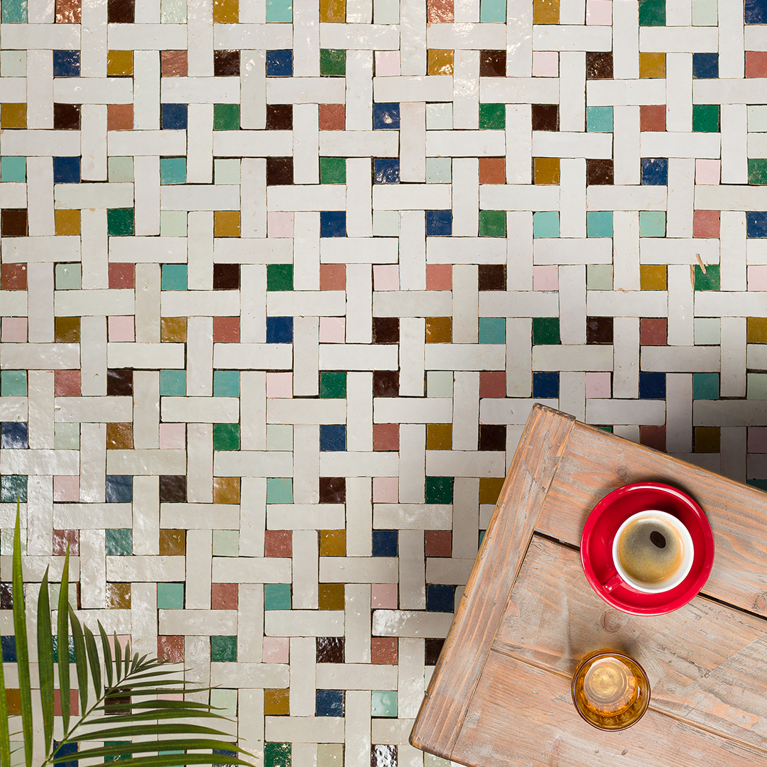 Colorful woven-pattern tile floor made of white rectangular tiles interlaced with small squares in shades of teal, pink, yellow, brown, and green. 