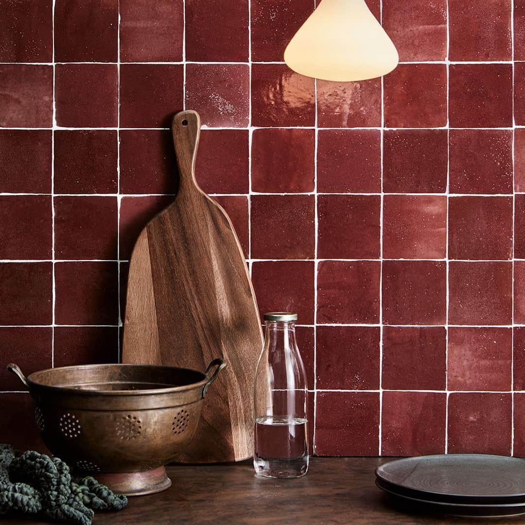 A kitchen countertop scene with glossy dark red square tiles and white grout.