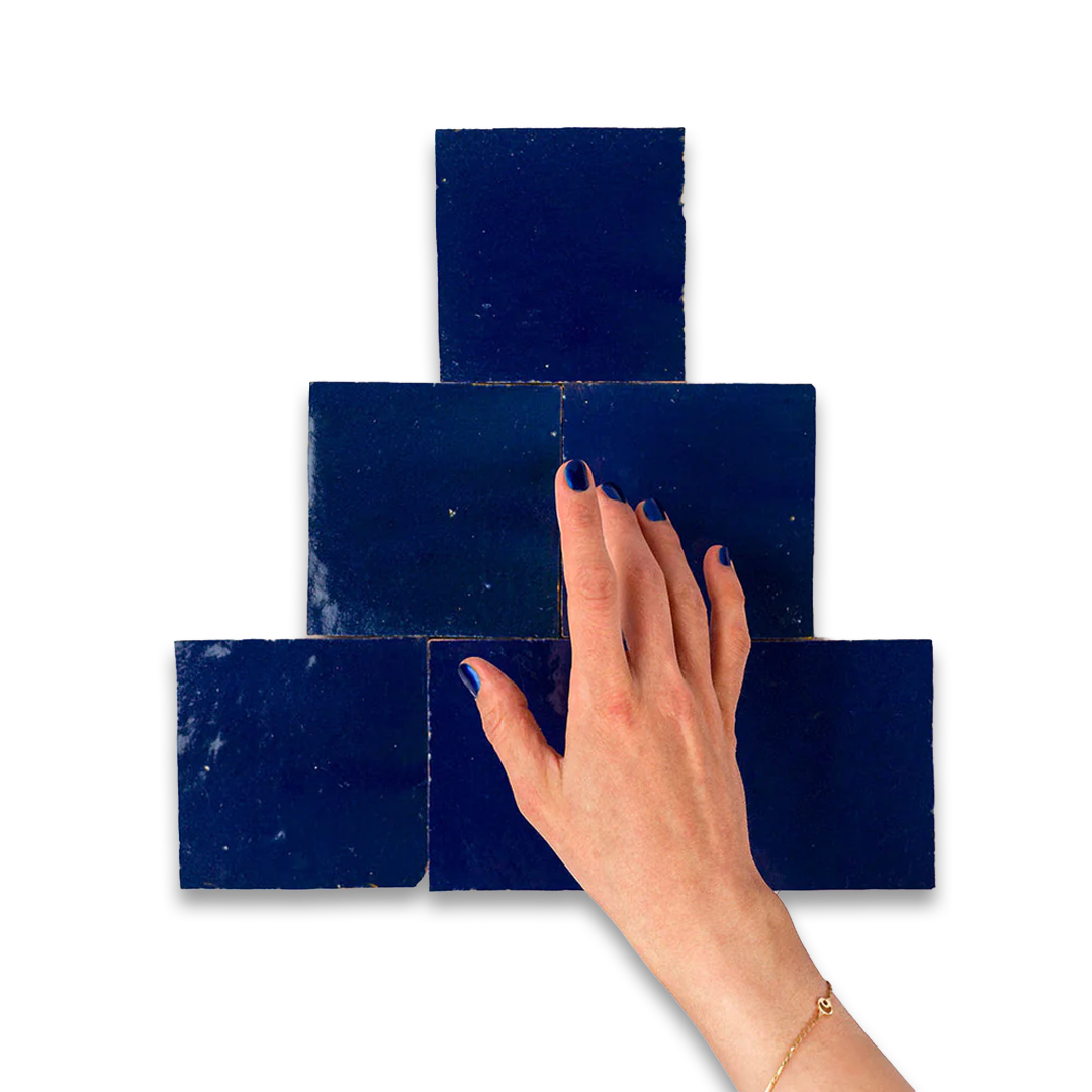 Hand with painted nails touching a set of blue square tiles on a white background