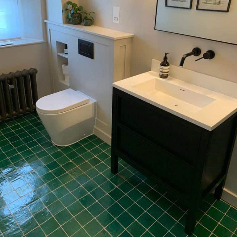 Modern bathroom with green tiled floors, a white toilet, black vanity with a white sink, and a sleek black faucet.