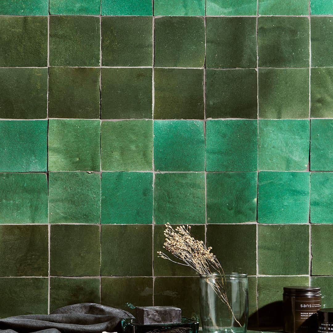 Close-up of green square tiles arranged in a checkerboard pattern, with dried flowers and decorative objects on the surface below.