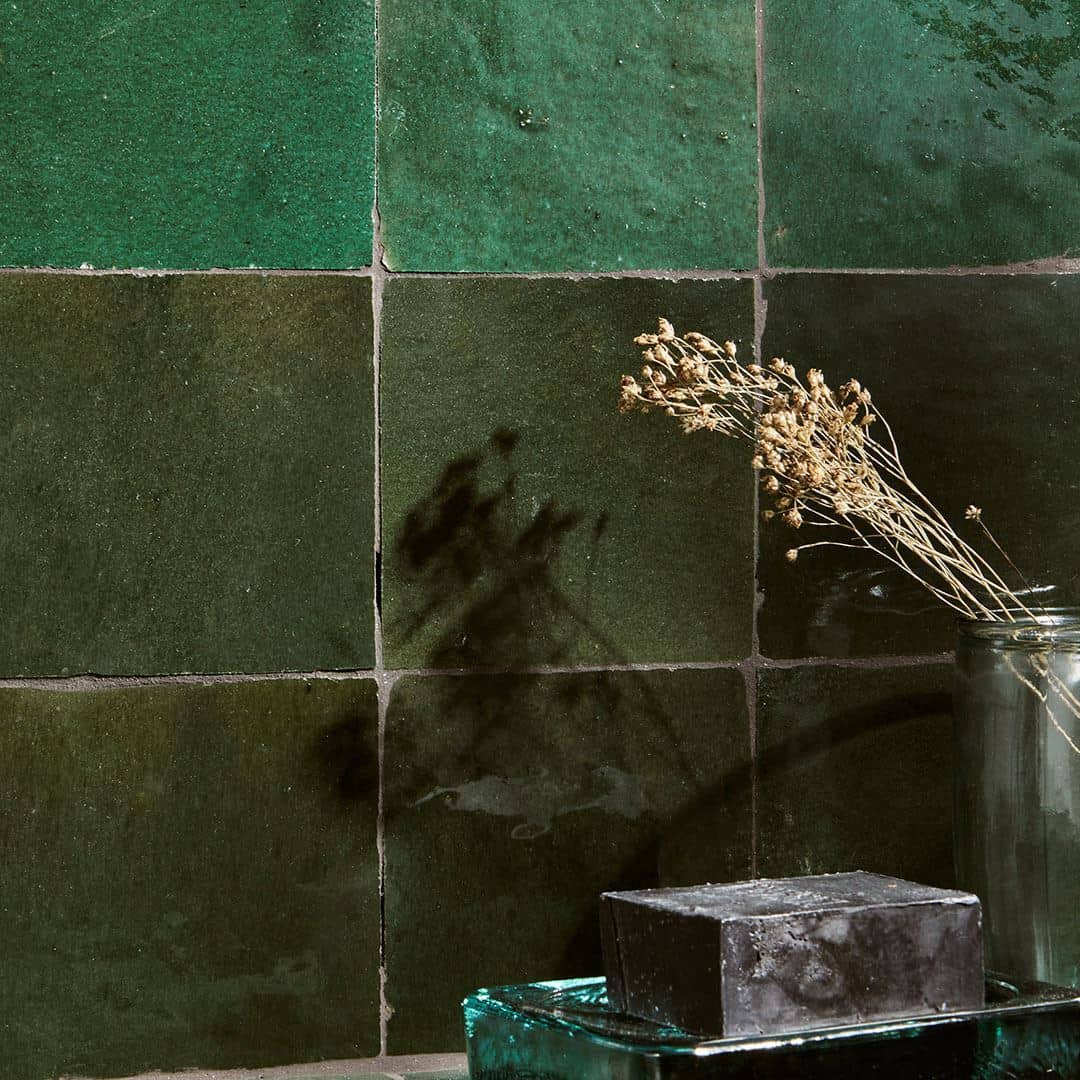 Close-up of green square tiles arranged in a checkerboard pattern, with dried flowers and decorative objects on the surface below.
