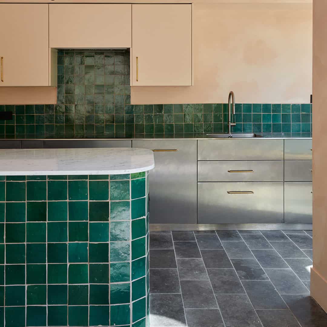 Modern kitchen with green square tiles on the walls and curved counter, stainless steel cabinets, and sleek faucet.