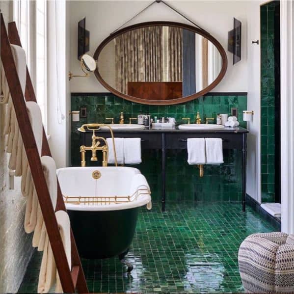 Luxurious bathroom with a black and gold freestanding bathtub, green tiled walls, double sink vanity, and an elegant oval mirror.