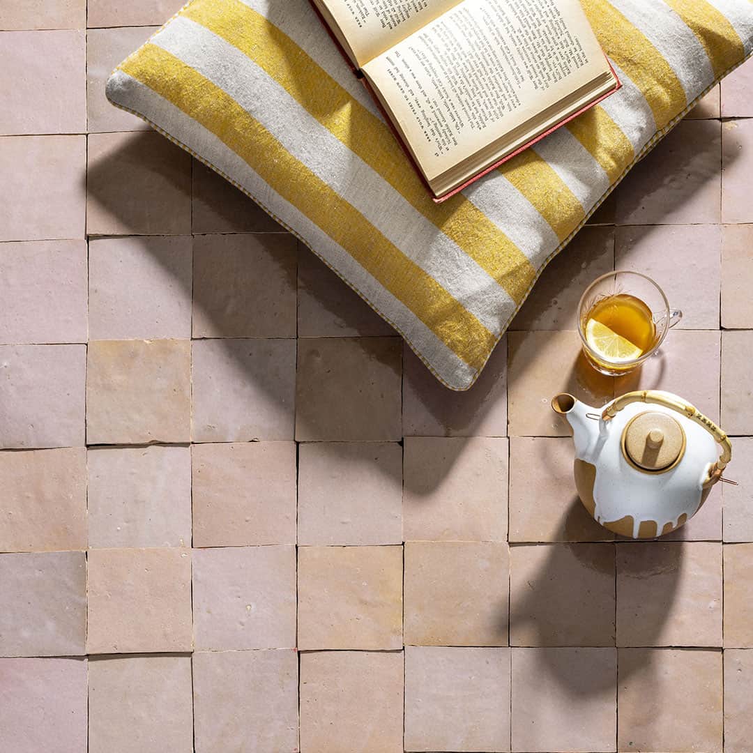 A cozy scene on a tiled beige surface with a striped yellow-and-white cushion holding an open book.