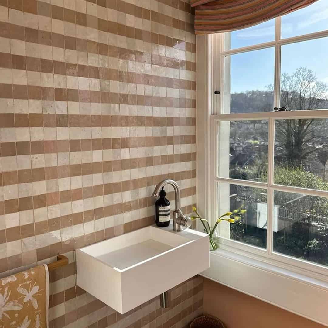 A small modern bathroom with a rectangular white wall-mounted sink beneath a window. 