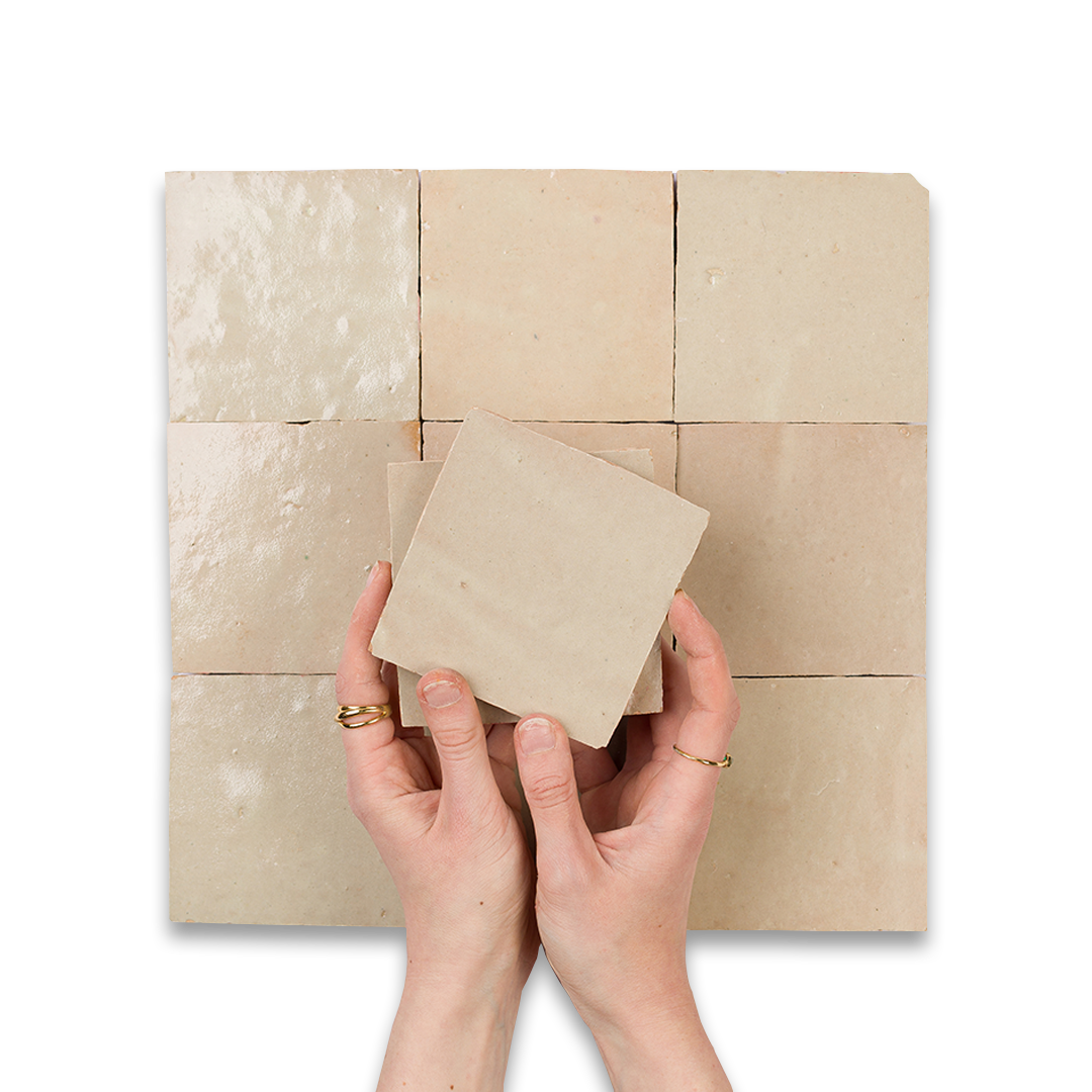 Hands holding a tile sample in front of a wall of different tile patterns.
