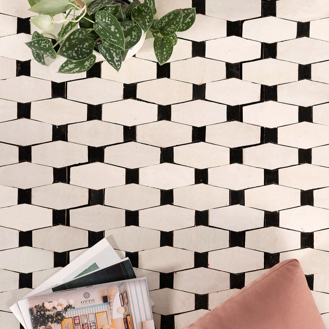 Black and white geometric tile pattern with a plant and magazine on a surface.