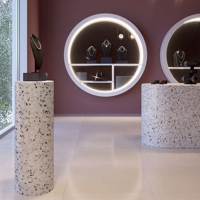 Modern jewelry display with terrazzo pedestals, pearl necklace on black bust, illuminated circular wall cases showcasing necklaces, mauve walls, and polished light floor