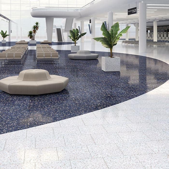 Spacious modern airport terminal with terrazzo flooring, circular beige seating, large glass windows, tropical potted plants, and overhead signage for gates 11–21.