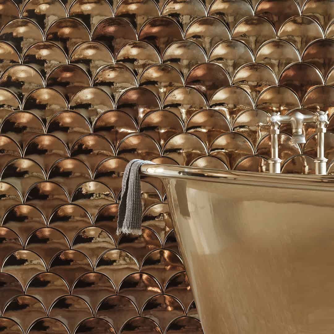Metallic gold scallop tile wall with freestanding bathtub and chrome fixtures in luxury bathroom.