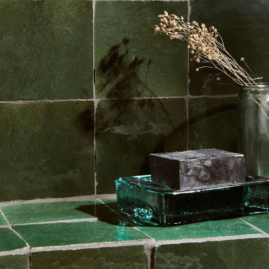 Close-up of green tiled wall with a glass container holding a soap bar and dried flowers, creating a minimalist bathroom aesthetic.