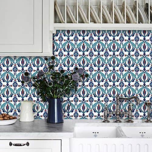 Kitchen backsplash with intricate blue and teal patterned tiles, white cabinets, farmhouse sink, and decorative vase.