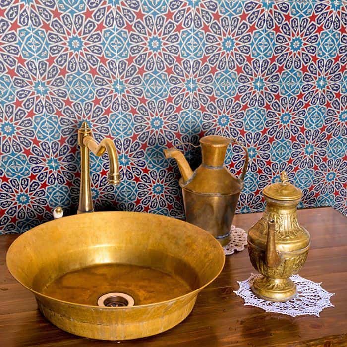 Brass vessel sink with matching faucet and decorative metalware against colorful geometric tile backsplash.